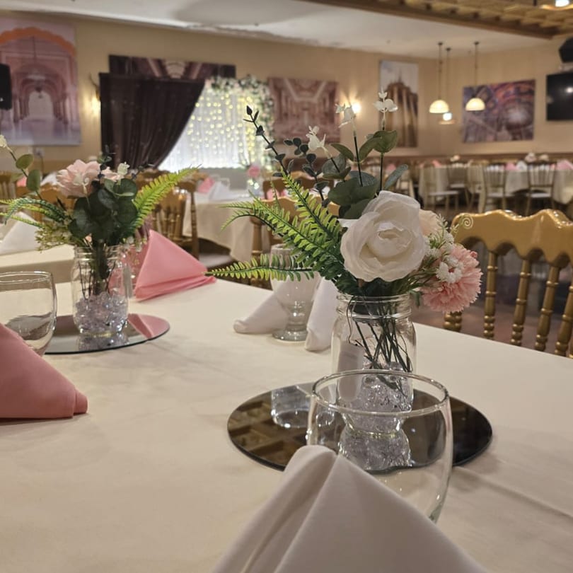 Elegant dining room at Spice Culture with tables set with floral centerpieces, pink napkins, and golden chairs.