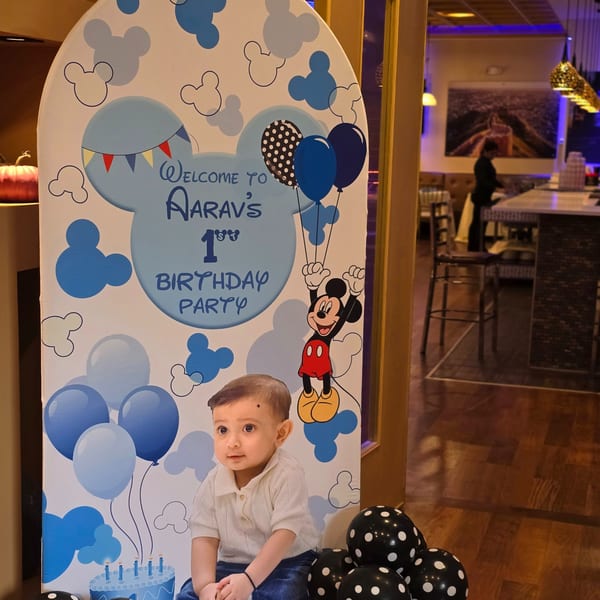 A Mickey Mouse themed birthday sign for Aarav's 1st birthday party, with a baby's picture.