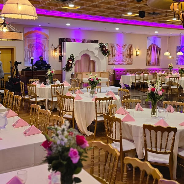 An Indian restaurant dining room with tables set for an event, featuring a stage and DJ booth.
