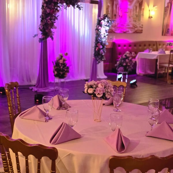 A round table set with pink napkins and a floral centerpiece, bathed in purple lighting.