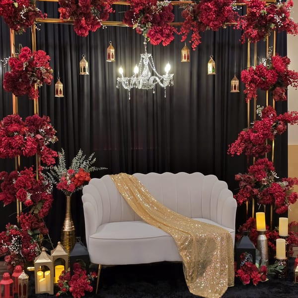 Elegant white sofa with a gold sequin throw, surrounded by red floral arrangements and lanterns.