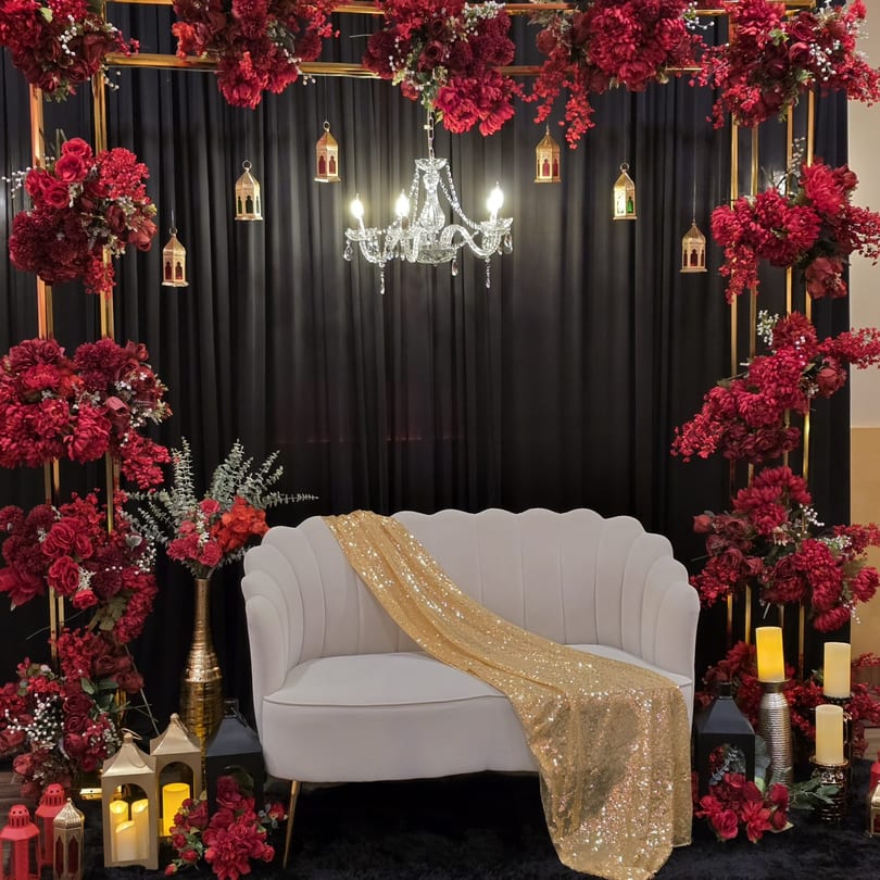 Elegant white sofa with a gold sequin throw, surrounded by red floral arrangements and lanterns.