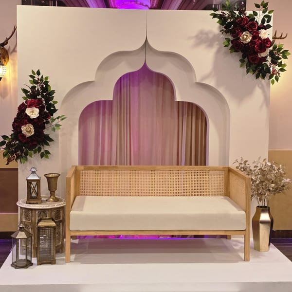 An Indian-inspired seating area with a wooden bench, archway, floral arrangements, and lanterns.