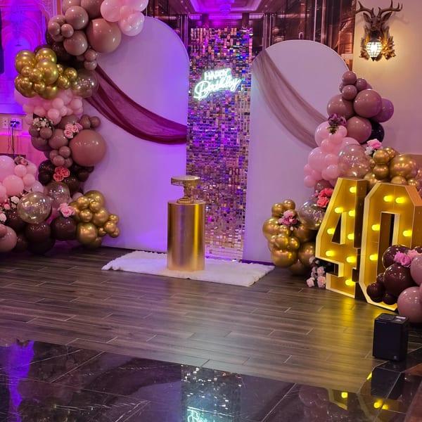 A birthday party setup with pink, gold, and brown balloons, a "Happy Birthday" neon sign, and illuminated "40" numbers.