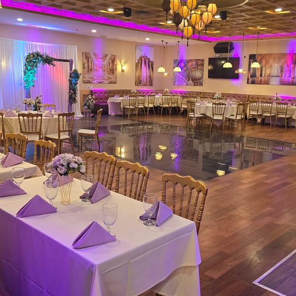 Elegant Indian restaurant interior with tables set, floral arch, and purple lighting for an event.
