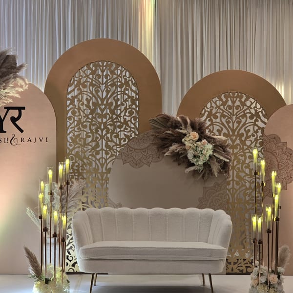 Elegant Indian wedding stage with a white sofa, golden arch backdrops, floral arrangements, and candle-like lights.