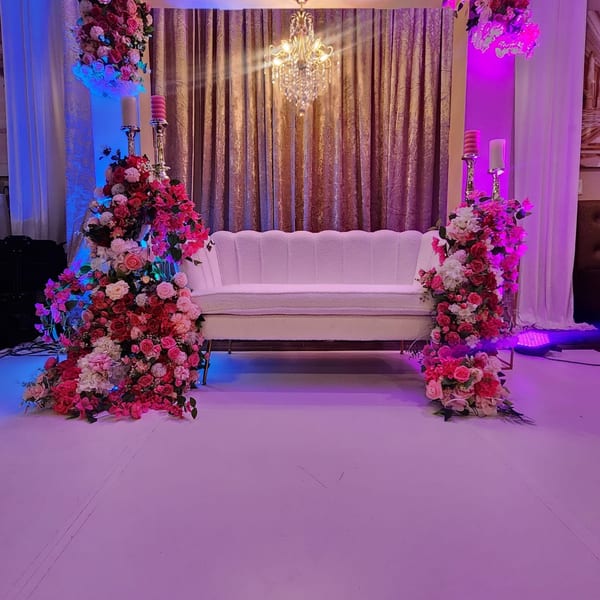 Elegant white sofa flanked by tall floral arrangements and candelabras, set against a gold curtain backdrop.
