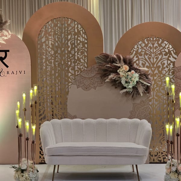 Elegant Indian wedding stage with a white sofa, floral arrangements, and decorative gold screens.