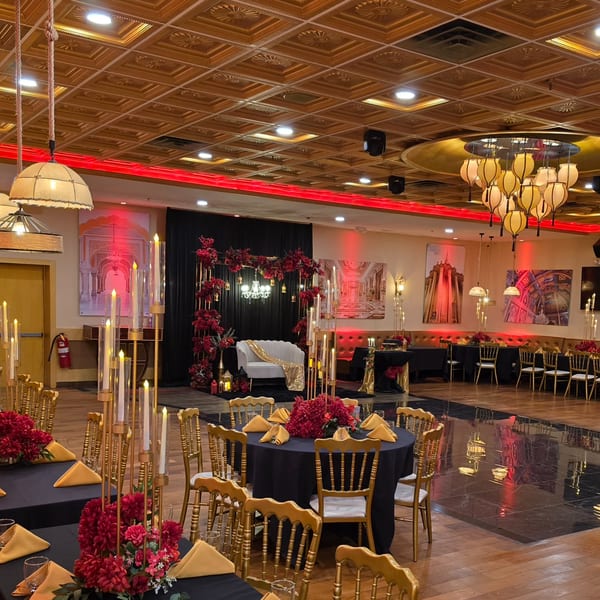 Elegant Indian restaurant interior with black and gold tables, red floral centerpieces, and a stage with a white couch.