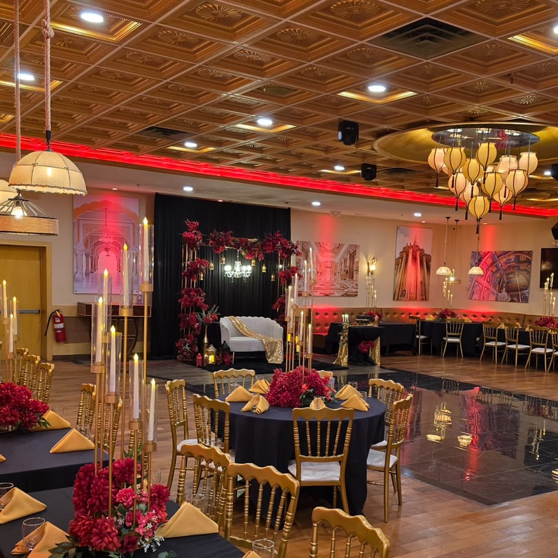 Elegant Indian restaurant interior with black and gold tables, red floral centerpieces, and a stage with a white couch.