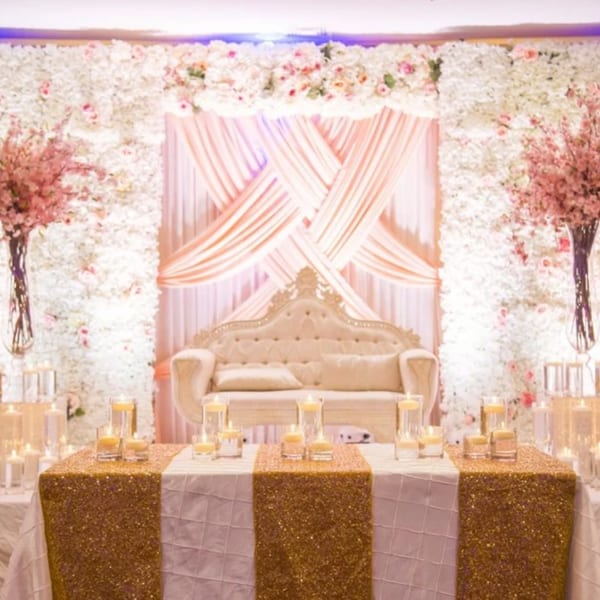 Elegant Indian wedding stage with a white sofa, floral wall, and candlelit golden table.