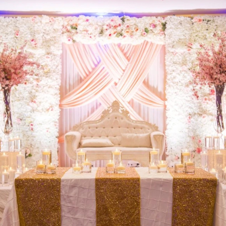 Elegant Indian wedding stage with a white sofa, floral wall, and candlelit golden table.