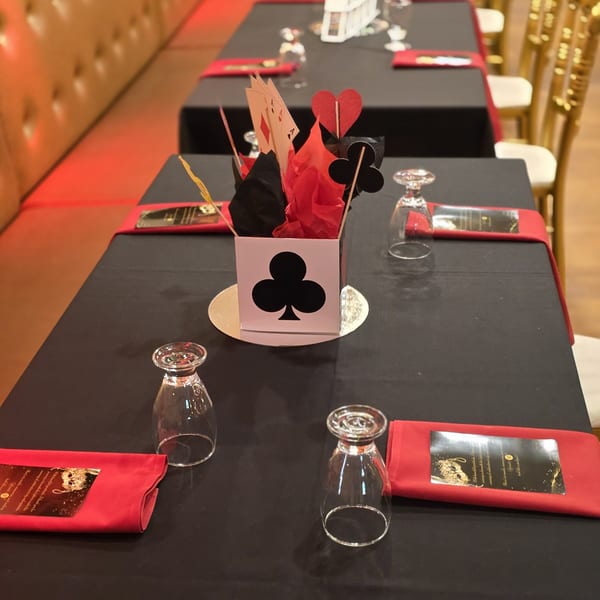 Table set with black tablecloths, red napkins, inverted glasses, and a playing card themed centerpiece.