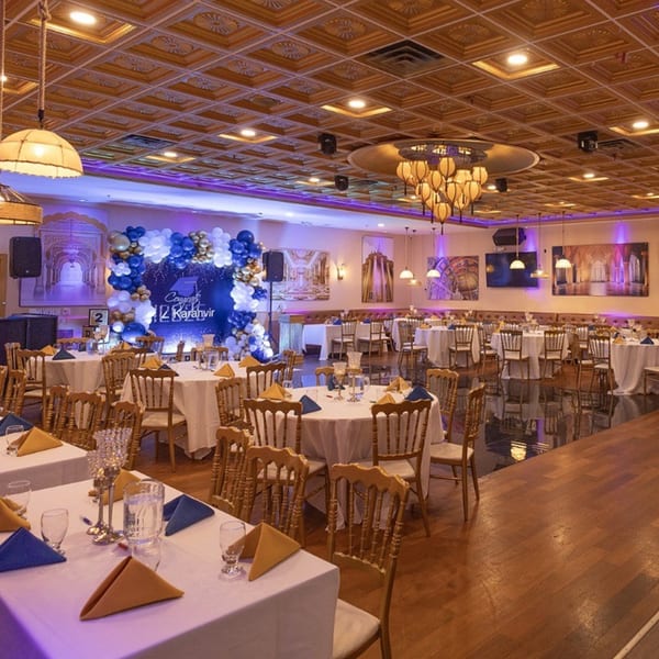 A large event hall at Spice Culture with round tables set for guests and a blue and gold balloon arch.