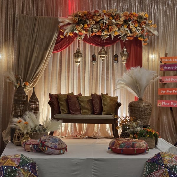 An Indian-themed event space with a sofa, decorative pillows, lanterns, and floral arrangements.