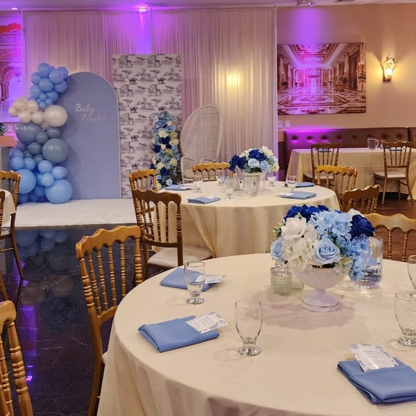 A decorated dining room with round tables set with blue napkins and floral centerpieces, ready for an event.