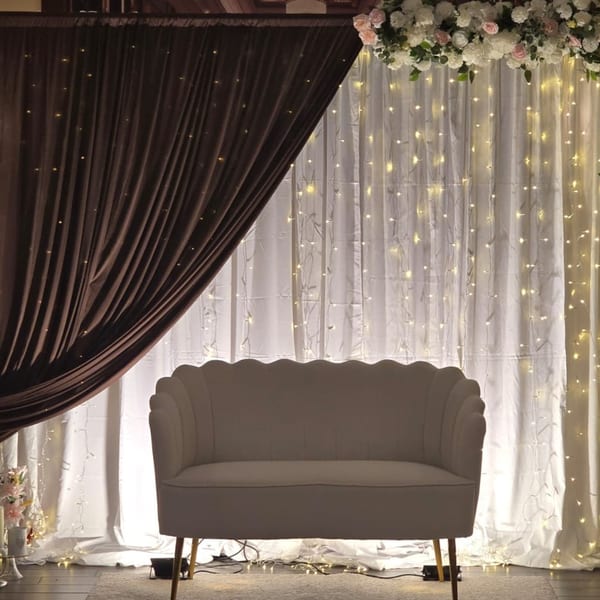 Elegant beige sofa in front of white curtains with string lights and floral arrangements.