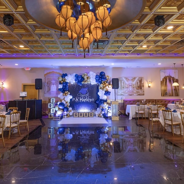 A decorated event space with a "Congrats P.A. Karanvir Grad" backdrop, balloons, and dining tables.