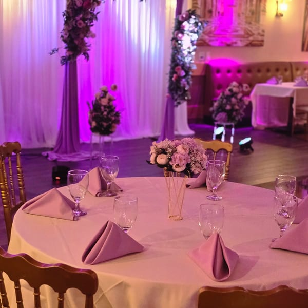 A dining table set with pink napkins and a floral centerpiece under purple lighting at Spice Culture.