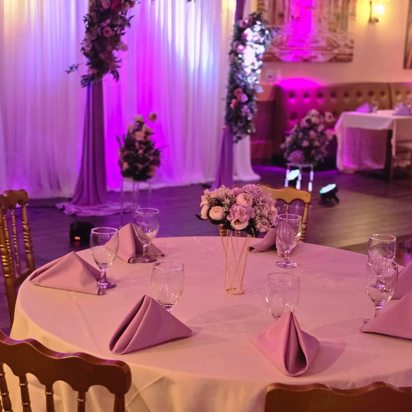 A dining table set with pink napkins and a floral centerpiece under purple lighting at Spice Culture.